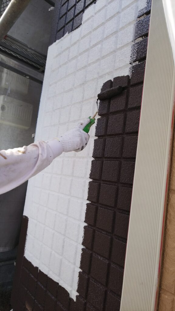丁寧な手作業で外壁にこげ茶色の塗料をローラー塗布中。しっかり密着し、美しい仕上がりへ。